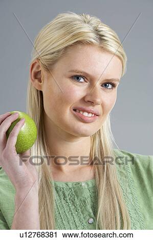 Stock Image - Woman Relaxing On Sofa Eating Apple At Home. Fotosearch