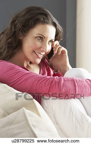 Stock Photography - Woman Relaxing Sitting On Sofa At Home Talking On Phone. Fotosearch