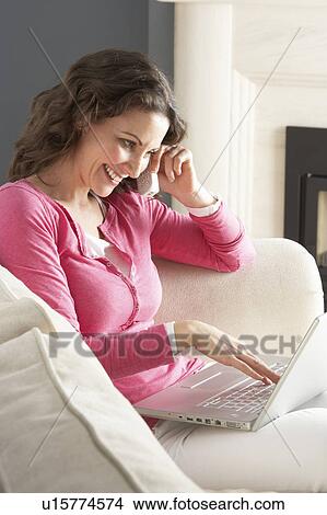 Woman Using Laptop Relaxing Sitting On Sofa At Home Talking On Phone View Large Photo Image Picture - Woman Using Laptop Relaxing Sitting On Sofa At Home Talking On Phone. Fotosearch