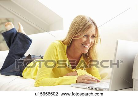 Stock Image - Woman Using Laptop Relaxing Sitting On Sofa At Home. Fotosearch