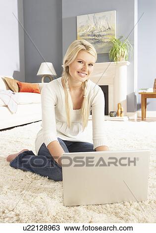 Stock Image - Woman Using Laptop Relaxing Sitting On Rug At Home. Fotosearch