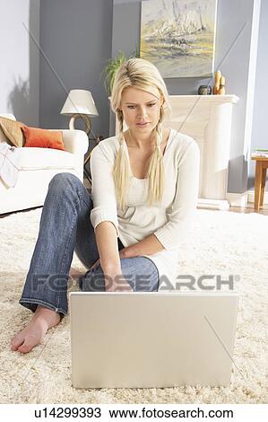 Stock Image - Woman Using Laptop To Manage Household Bills Laying On Rug At Home . Fotosearch