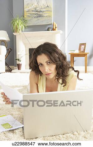 Stock Photo - Woman Using Laptop To Manage Household Bills Laying On Rug At Home . Fotosearch