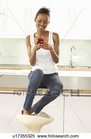 Stock Photography - Woman Using Mobile Phone Sitting In Modern Kitchen . Fotosearch