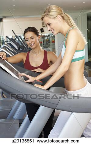 Stock Image - Woman Working With Female Personal Trainer On Running Machine In Gym. Fotosearch