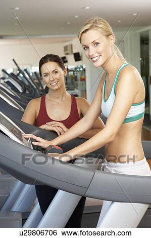 Stock Photograph - Woman Working With Female Personal Trainer On Running Machine In Gym. Fotosearch
