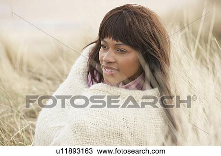 Stock Image - Woman Wrapped In Blanket Amongst Dunes On Winter Beach. Fotosearch