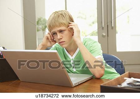 Stock Image - Worried Looking Teenage Boy Using Laptop At Home. Fotosearch