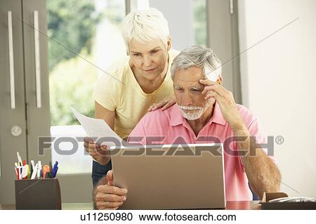 Stock Image - Worried Senior Couple Using Laptop At Home. Fotosearch