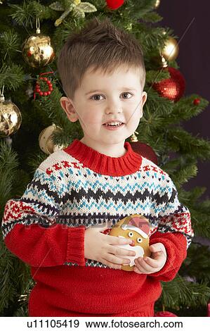Stock Photo - Young Boy Eating Cookie In Front Of Christmas Tree. Fotosearch