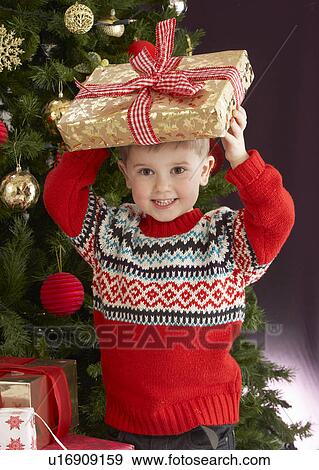 Stock Photo - Young Boy Holding Christmas Present In Front Of Christmas Tree. Fotosearch
