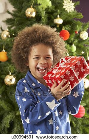 Young Boy Holding Gift In Front Of Christmas Tree View Large Photo Image Stock Image - Young Boy Holding Gift In Front Of Christmas Tree. Fotosearch