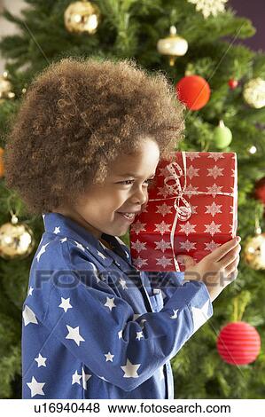 Young Boy Holding Gift In Front Of Christmas Tree View Large Photo Image Stock Photo - Young Boy Holding Gift In Front Of Christmas Tree. Fotosearch