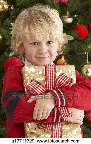 Young Boy Holding Gift In Front Of Christmas Tree View Large Photo Image Stock Photo - Young Boy Holding Gift In Front Of Christmas Tree. Fotosearch