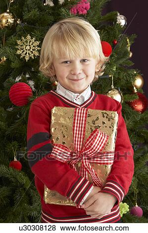 Young Boy Holding Gift In Front Of Christmas Tree View Large Photo Image Stock Photo - Young Boy Holding Gift In Front Of Christmas Tree. Fotosearch