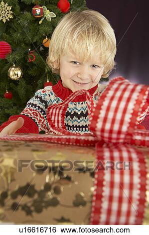 Young Boy Holding Gift In Front Of Christmas Tree View Large Photo Image Stock Photograph - Young Boy Holding Gift In Front Of Christmas Tree. Fotosearch