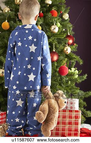 Stock Photo - Young Boy Holding Teddy Bear In Front Of Christmas Tree. Fotosearch