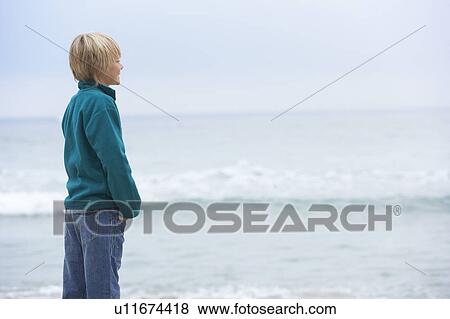 Stock Photo - Young Boy On Holiday Standing On Winter Beach Looking Out To Sea. Fotosearch