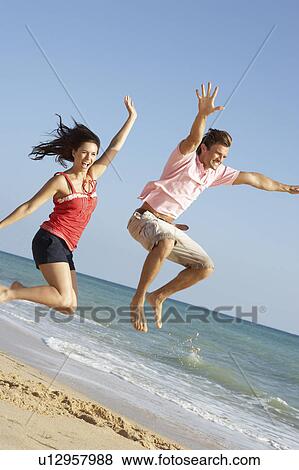 Young Couple Enjoying Beach Holiday Jumping In Air View Large Photo Image Stock Photo - Young Couple Enjoying Beach Holiday Jumping In Air. Fotosearch