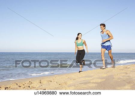 Stock Image - Young Couple In Fitness Clothing Running Along Beach. Fotosearch