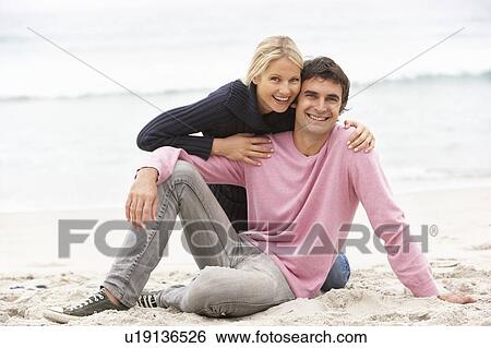 Stock Photograph - Young Couple On Holiday Sitting On Winter Beach. Fotosearch