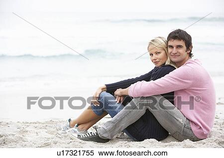 Stock Photography - Young Couple On Holiday Sitting On Winter Beach. Fotosearch