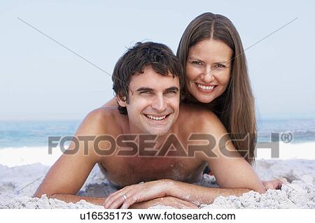 Stock Image - Young Couple Relaxing On Beach Wearing Swimwear. Fotosearch