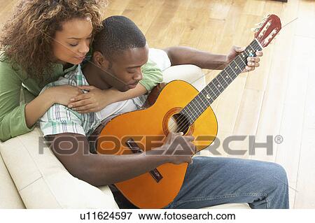 Young Couple Relaxing Sitting On Sofa Playing Acoustic Guitar View Large Photo Image Stock Photo - Young Couple Relaxing Sitting On Sofa Playing Acoustic Guitar. Fotosearch