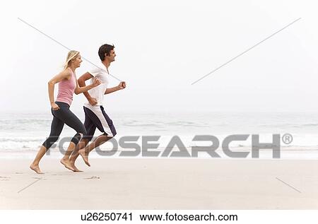 Stock Image - Young Couple Running Along Winter Beach. Fotosearch