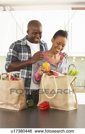 Stock Photograph - Young Couple Unpacking Shopping In Modern Kitchen . Fotosearch
