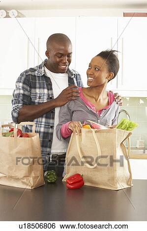 Stock Photograph - Young Couple Unpacking Shopping In Modern Kitchen . Fotosearch