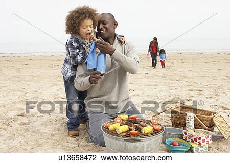 Stock Image - Young Family Enjoying Barbeque On Beach. Fotosearch
