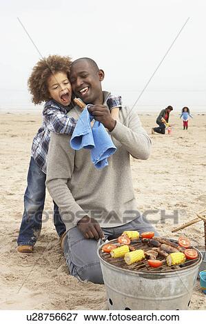 Stock Photo - Young Family Enjoying Barbeque On Beach. Fotosearch