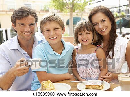 Stock Image - Young Family Enjoying Cup Of Coffee And Cake In Café Together. Fotosearch