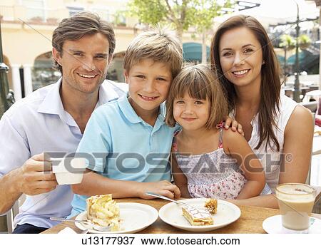 Stock Photo - Young Family Enjoying Cup Of Coffee And Cake In Café Together. Fotosearch