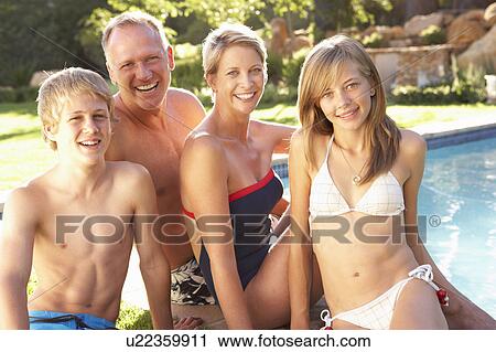 Stock Image - Young Family Relaxing By Pool In Garden. Fotosearch
