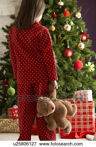 Stock Photo - Young Girl Standing With Teddy Bear In Front Of Christmas Tree. Fotosearch