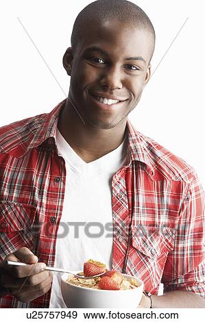 Stock Photo - Young Man Eating Bowl Of Healthy Breakfast Cereal In Studio. Fotosearch