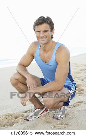 Stock Photography - Young Man In Fitness Clothing Resting After Exercise On Beach. Fotosearch