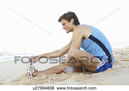 Stock Photo - Young Man In Fitness Clothing Stretching On Beach. Fotosearch