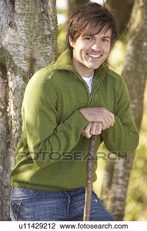Stock Image - Young Man Outdoors Walking In Autumn Woodland Holding Walking Stick. Fotosearch
