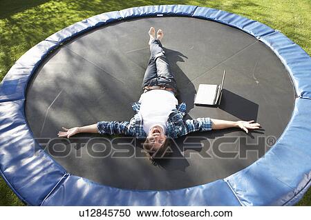 Stock Image - Young Man Relaxing On Trampoline With Laptop. Fotosearch