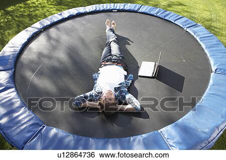 Stock Photograph - Young Man Relaxing On Trampoline With Laptop. Fotosearch