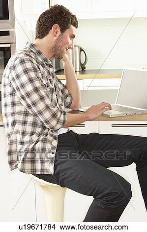 Picture - Young Man Relaxing Sitting In Kitchen Talking On Phone. Fotosearch
