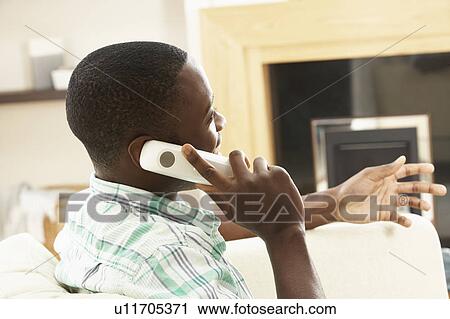 Stock Image - Young Man Relaxing Sitting On Sofa At Home Talking On Phone. Fotosearch