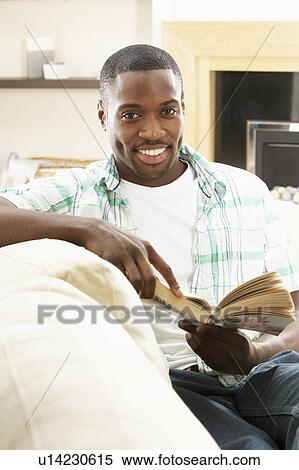 Stock Photography - Young Man Relaxing Sitting On Sofa Reading Book At Home. Fotosearch
