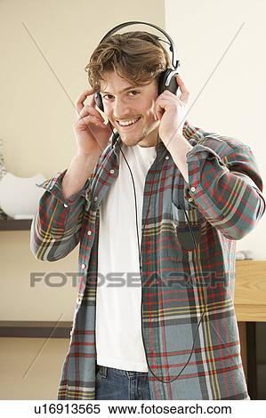 Stock Photography - Young Man Relaxing Sitting On Sofa Listening to Music At Home On Headphones. Fotosearch