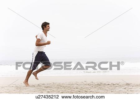 Stock Image - Young Man Running Along Winter Beach. Fotosearch
