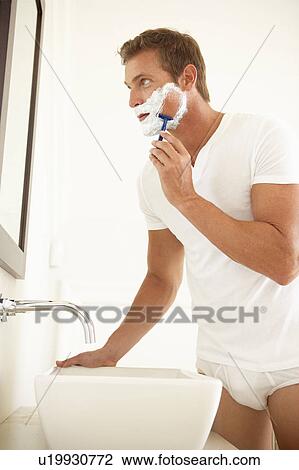 Stock Image - Young Man Shaving In Bathroom Mirror. Fotosearch