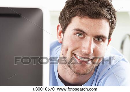 Stock Image - Young Man Using Computer In Modern Kitchen . Fotosearch